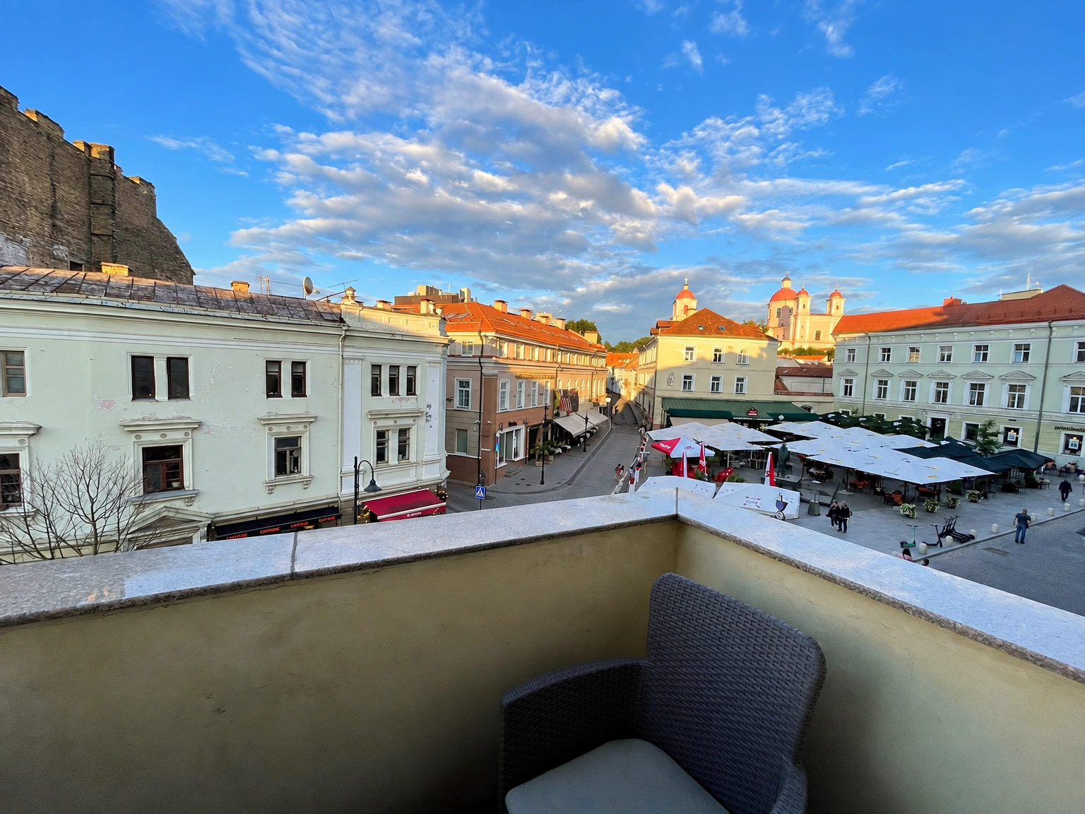 Ein Balkon mit einem Sessel und Blick auf den Stadtplatz sowie die umliegenden Gebäude.