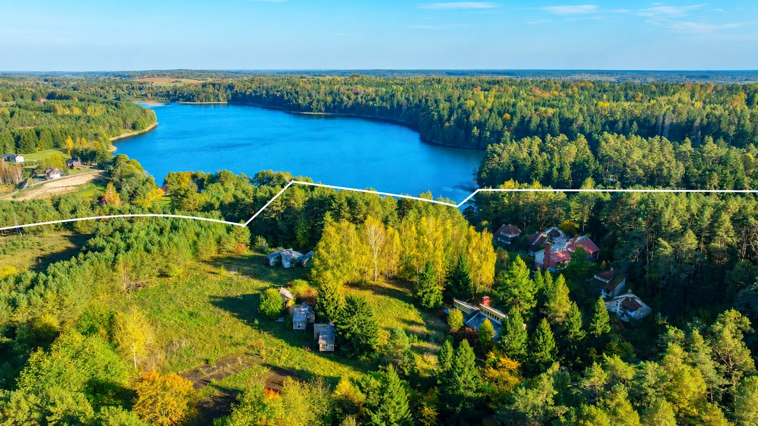 Von oben sind ein See, ein Wald und zwischen den Bäumen gelegene Häuser zu sehen.