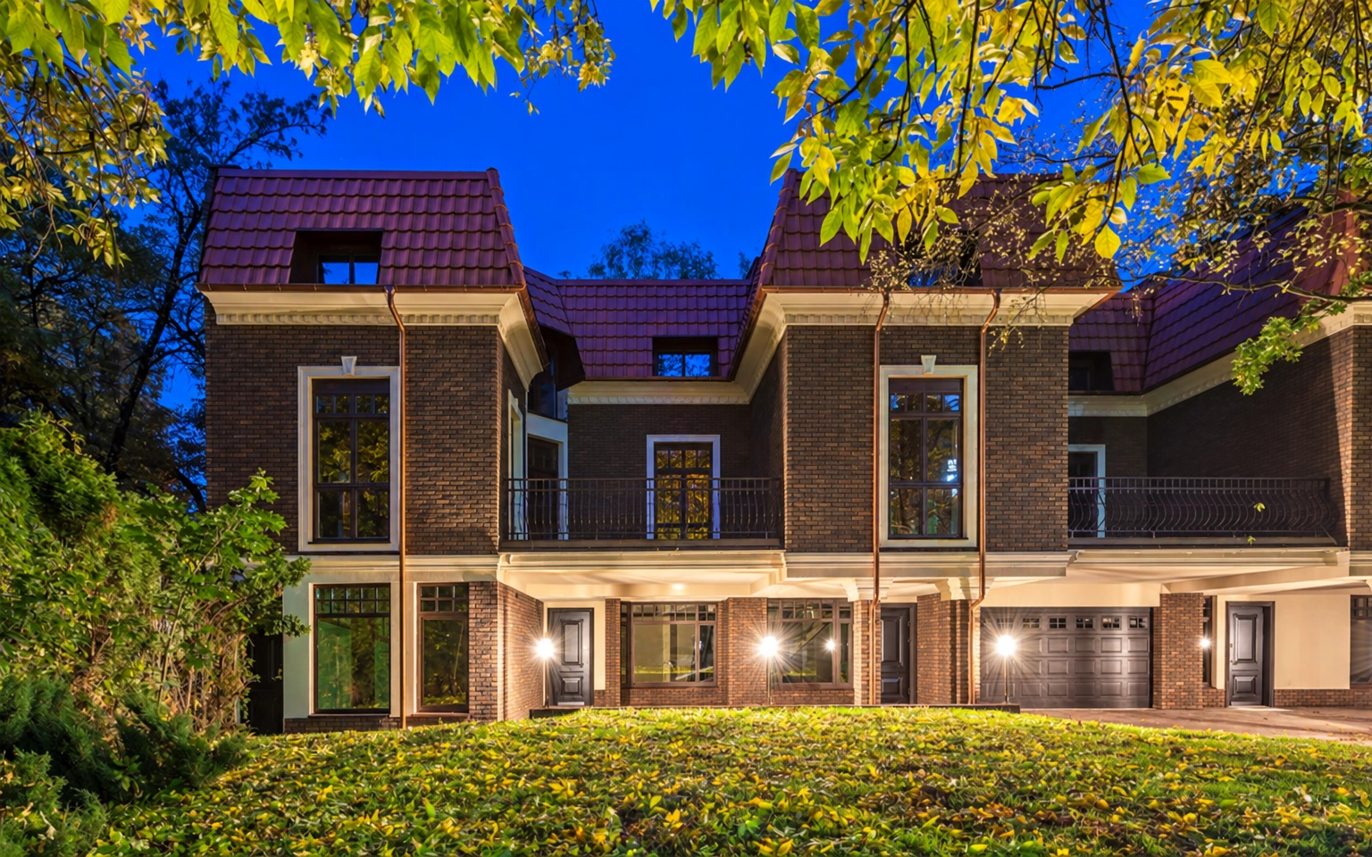 Die Fassade des Gebäudes mit großen Fenstern und einem Schrägdach; davor erstreckt sich eine Rasenfläche.