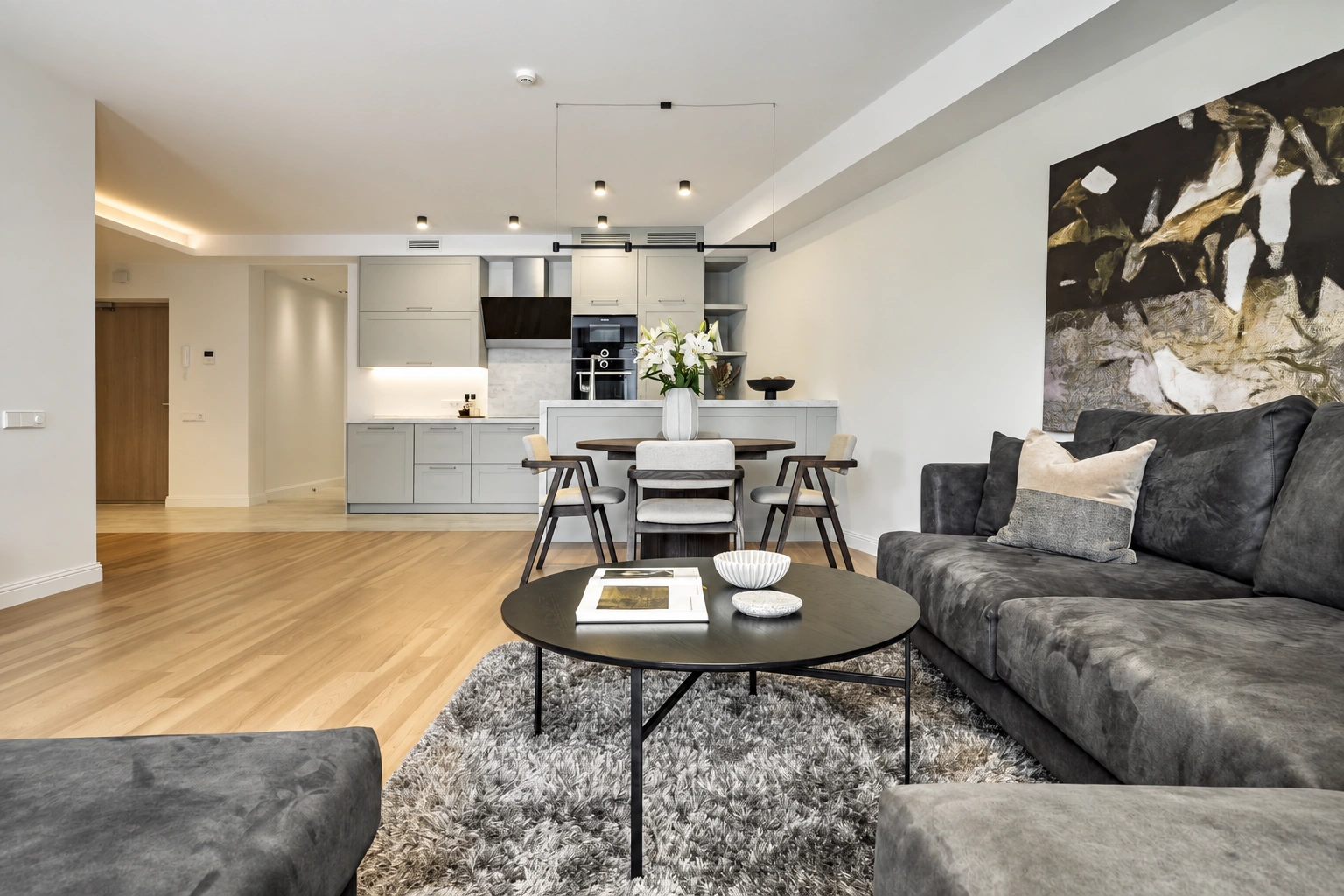 Im Wohnzimmer stehen ein graues Sofa und ein runder Couchtisch, und im Hintergrund ist der Küchenbereich zu sehen.